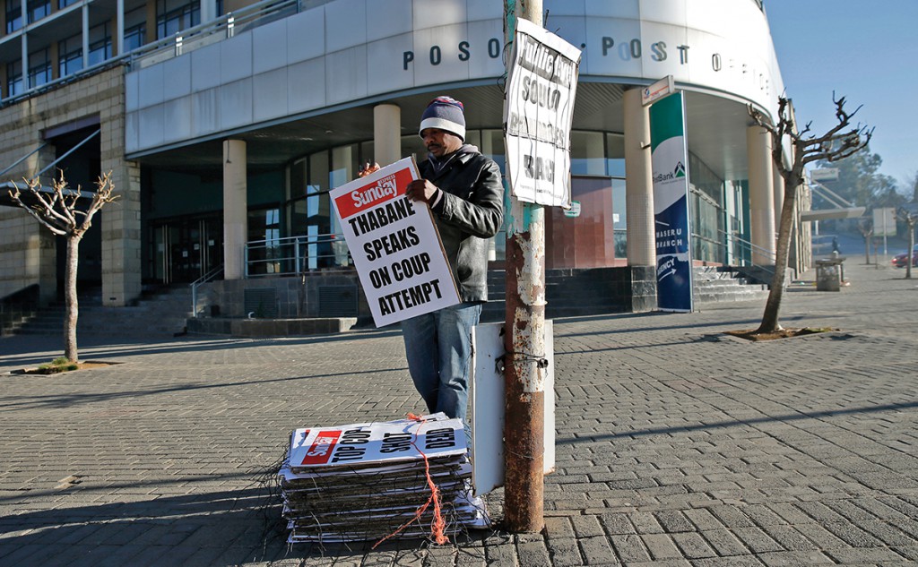 A worker hangs posters displaying newspaper headlines, in the capital Maseru