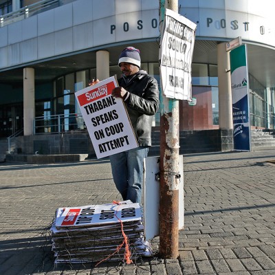 A worker hangs posters displaying newspaper headlines, in the capital Maseru