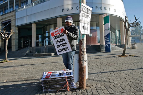 A worker hangs posters displaying newspaper headlines, in the capital Maseru