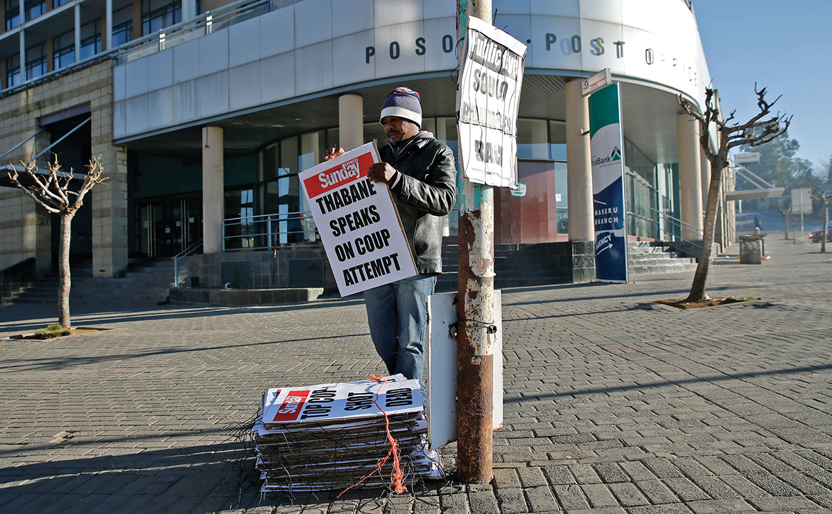 A worker hangs posters displaying newspaper headlines, in the capital Maseru