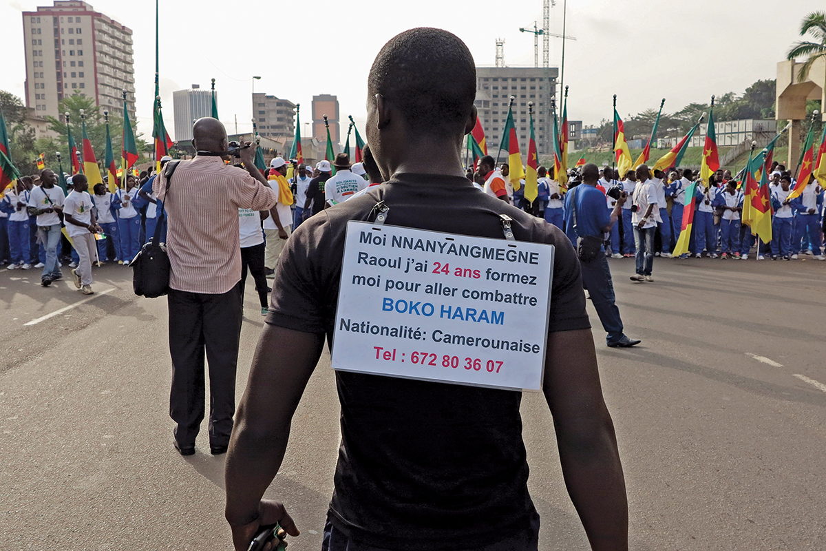 A man wears a sign on his back with his request to be trained and sent to the front line to fight against Boko Haram